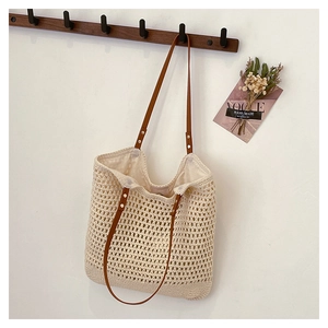 Detail of the woven hollow pattern and brown leather straps on the cream beach tote bag