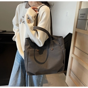 Detail view of large dark grey canvas tote bag with side pockets and metal button detail