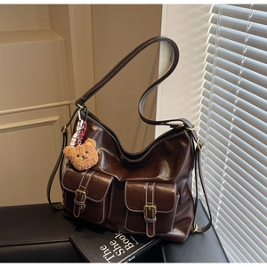 Detail of dark brown leather tote bag featuring functional front pockets and a bear charm