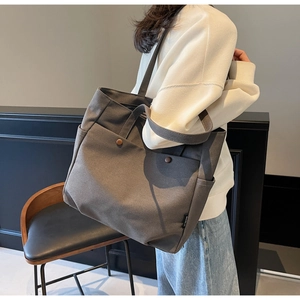 Detail of dark grey canvas tote bag showing bronze rivets and side storage pocket texture