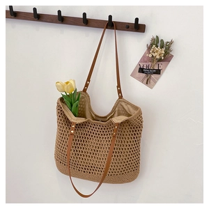 Detail of hollow woven beige straw tote with brown leather strap and rivet accents