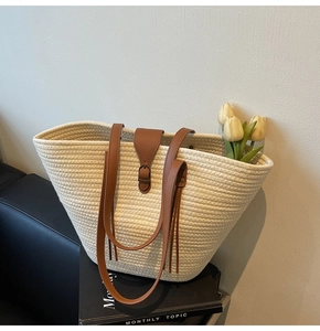 Detailed view of cream straw tote bag with brown faux leather straps and buckle closure