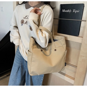 Detail of khaki canvas tote bag featuring large front pockets and blue striped lining