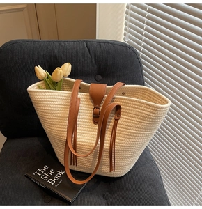 Close-up of woven straw tote bag with brown leather strap and vintage buckle detail