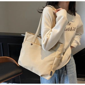 Detail of beige canvas tote bag showing side storage pocket and brand label on shoulder