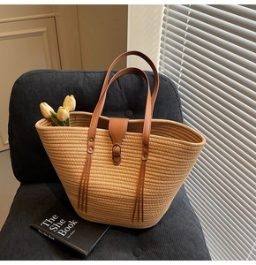 Detail of a large straw tote bag with brown leather handles on a blue velvet chair