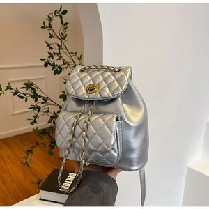 Détail du sac à dos argenté matelassé avec fermoir rotatif doré et bandoulière en chaîne