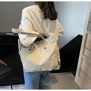 Detail of beige canvas tote bag with striped lining and large front pocket shown on model