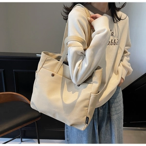 Detail of beige canvas tote bag showing brown button pockets and side brand label