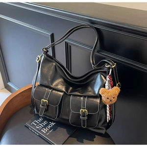 Detail of black leather tote bag with white contrast stitching and plush bear charm