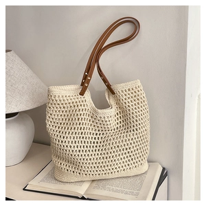 Detail of hollow mesh crochet texture and brown leather straps on beige beach tote bag