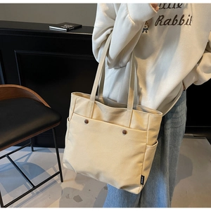 Detail of beige canvas tote bag featuring front pocket and brown decorative buckle