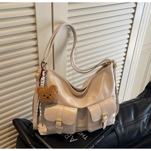Close-up of beige leather hobo bag with front buckle pockets and brown bear charm