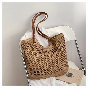 Detail of hollow woven straw tote bag with brown leather handles on a white chair