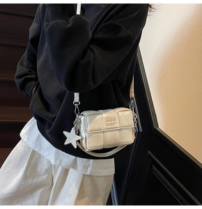 Détail d'un sac bandoulière beige tissé avec pendentif étoile porté par un mannequin stylé