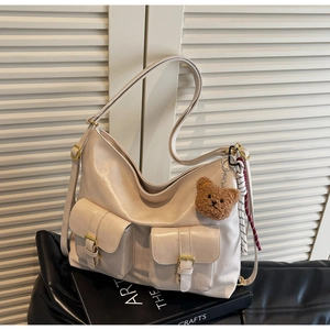 Detail of beige tote bag featuring double buckled pockets and cute bear charm