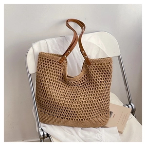 Detailed close-up of the hollow woven texture and brown leather handle on a straw tote bag
