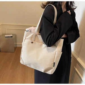 Detail of off-white canvas tote bag with front pocket and brown button accents