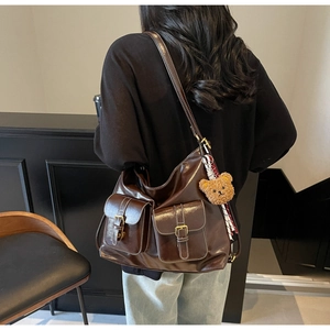 Detail of dark brown leather tote bag showing twin front pockets and teddy bear charm