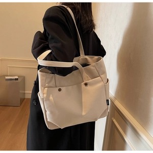 Detail of off-white canvas tote bag featuring side pockets and dark brown snap buttons