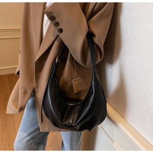 Detail of a black minimalist hobo bag with gold hardware shown on a model's shoulder