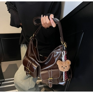 Detail of dark brown leather tote bag with functional pockets and a teddy bear charm
