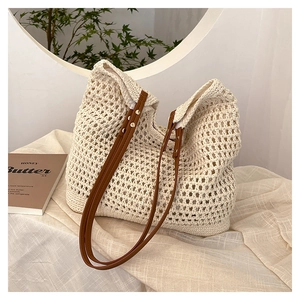 Close-up of woven hollow-out tote bag with brown leather handles on a minimal table