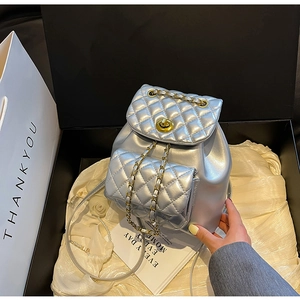 Détail du sac à dos argenté matelassé avec chaîne dorée dans une boîte cadeau