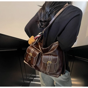Detail of dark brown vintage tote bag featuring dual front pockets and plush bear charm