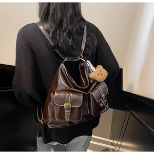 Detail of vintage brown leather backpack with buckle pockets and cute bear charm