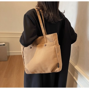 Detail view of the khaki canvas tote bag with front pocket and woven label on a model