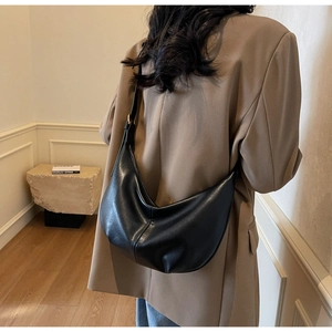 Detail of a large black leather hobo bag with soft pleated texture and wide strap