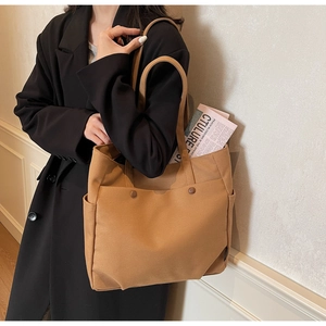 Detailed view of camel canvas tote bag with multi-pockets styled on a black coat