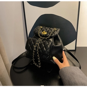 Détail d'un sac à dos noir matelassé avec fermoir doré et bandoulière chaîne