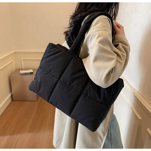 Model wearing a black quilted tote bag showcasing large capacity and minimalist puffer style