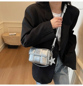 Détail d'un sac bandoulière argenté tressé avec breloque étoile et texture métallique