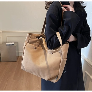 Detail view of khaki canvas tote bag featuring dual front pockets with snap buttons