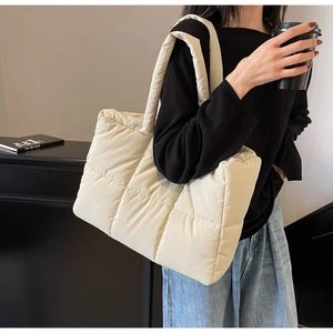 Detail of beige quilted tote bag showing padded texture and wide shoulder strap
