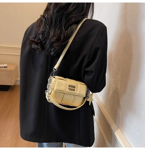 Modèle portant un sac bandoulière tressé jaune avec bandoulière chaîne et logo métal