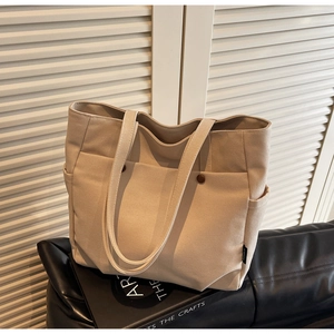 Detail view of beige canvas tote bag with front brown magnetic buckles and side pockets