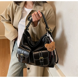 Detail of black tote bag with white stitching, outer pockets, and plush bear charm