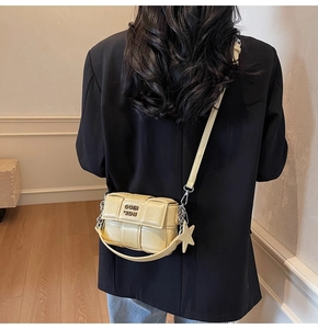 Détail du sac bandoulière beige tissé avec breloque étoile et plaque de marque en métal
