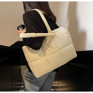 Detail view of quilted puffer tote bag in beige shown on shoulder in daily life