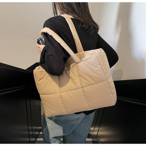 Close-up of khaki quilted tote bag on model showing soft padded texture and wide strap