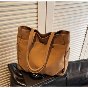 Detail view of brown canvas tote bag featuring front snap pockets and textured shoulder straps