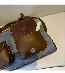 Detail view of denim and brown leather bag featuring a functional magnetic front pocket