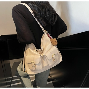 Detail of a large cream PU leather tote bag with functional front pockets and bear charm