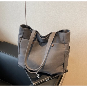 Grey canvas tote bag with brown button details resting on a sleek black leather chair
