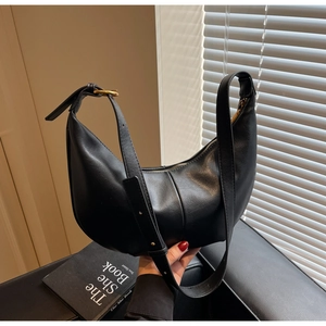 Detail of minimalist black leather dumpling bag with golden buckle on leather strap