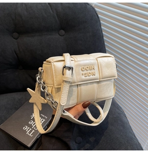 Détail du sac bandoulière tressé crème avec pendentif étoile et chaîne argentée en main